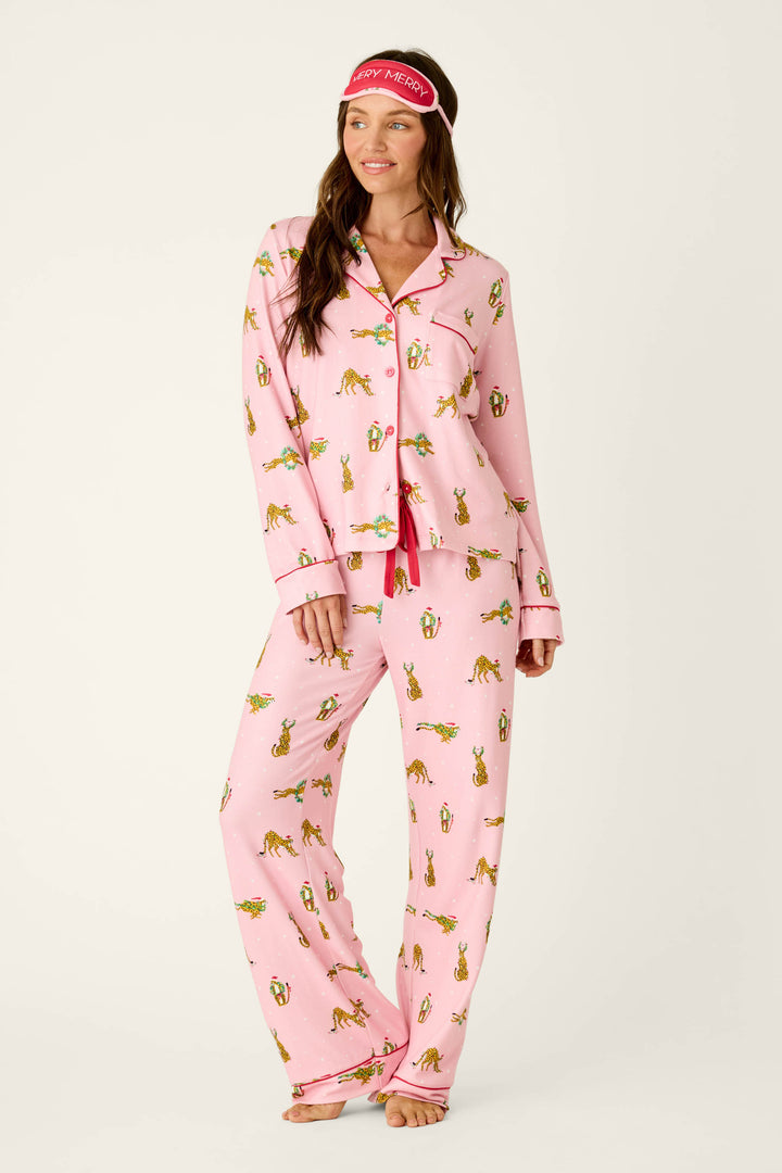 A woman wears a P.J. Salvage Very Merry Wild for the Holidays 3-Piece PJ Set featuring leopard print and animals in Santa hats, paired with a matching sleep mask on her forehead.