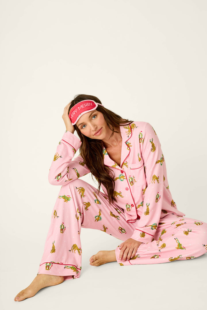 A woman wearing a P.J. Salvage Very Merry Wild for the Holidays 3-Piece PJ Set in leopard print with a matching sleep mask that reads Very Merry.