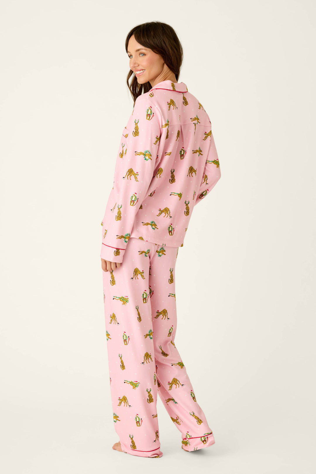 A woman stands and looks back wearing a pink P.J. Salvage Very Merry Wild for the Holidays 3-Piece PJ Set, featuring a pattern of leopards with holiday accessories and small white dots.