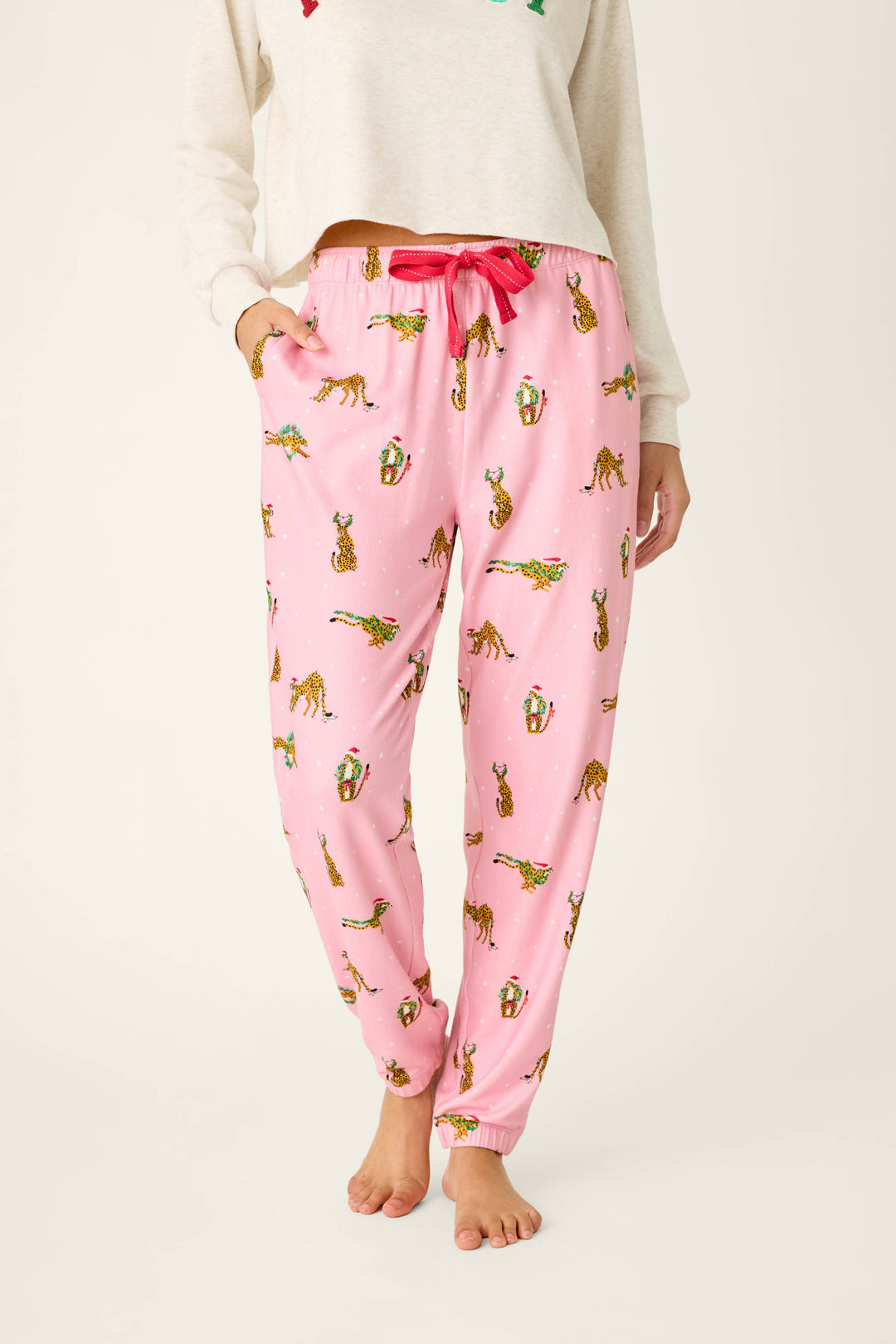 P.J. Salvage Very Merry Wild for the Holidays Jogger Pants in pink butter jersey, featuring a repeating pattern of leopards wearing Santa hats and festive greenery with a bright pink drawstring waistband.