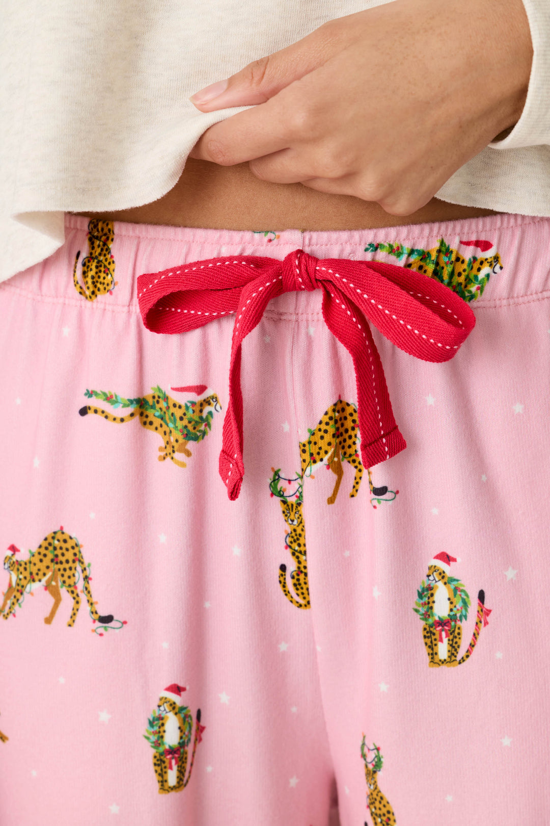 P.J. Salvage Very Merry Wild for the Holidays Jogger Pants in pink butter jersey, featuring a pattern of cheetahs wearing Santa hats and holiday wreaths, with a red drawstring waist.