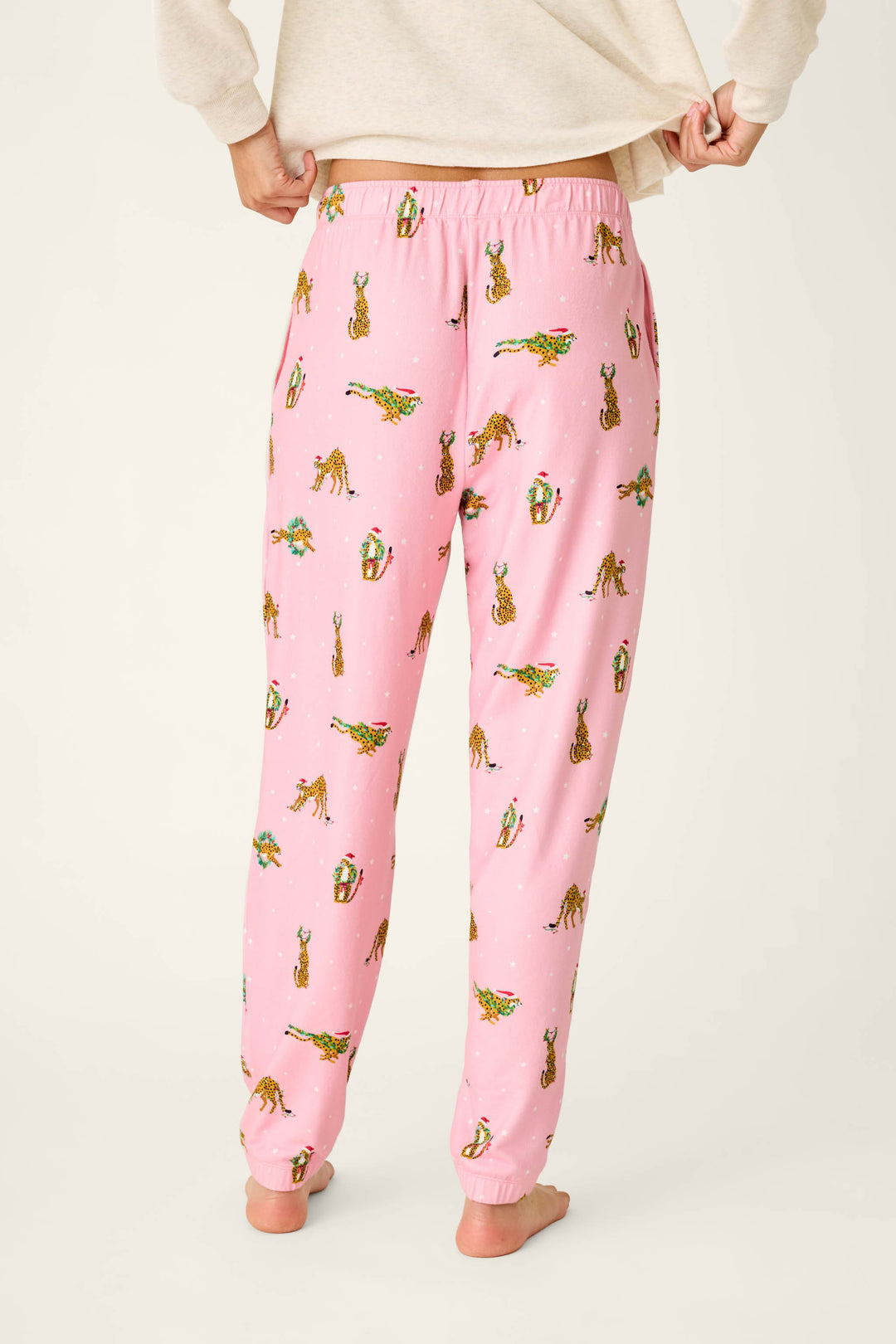 Person wearing pink P.J. Salvage Very Merry Wild for the Holidays Jogger Pants in a butter jersey fabric featuring a holiday-themed leopard print.