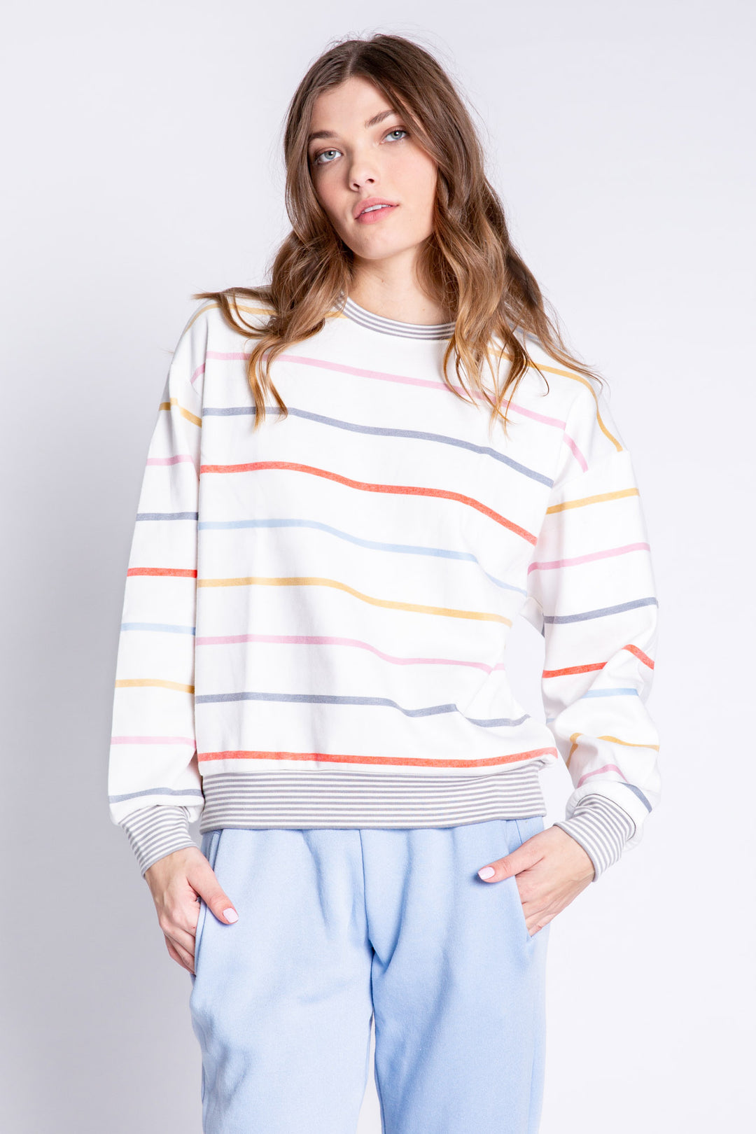 Woman wearing a colorful striped sweater and light blue pants on a plain background