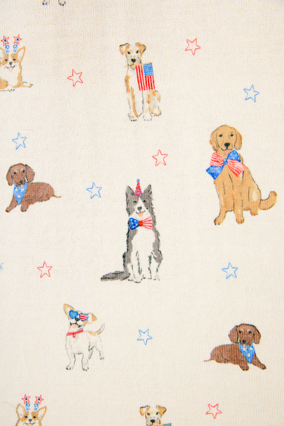 The P.J. Salvage Red, White, & Woof Patriotic Pups fabric features charming dogs in patriotic bows and hats with American flags, set on a ivory background with red and blue stars—ideal for Americana-inspired loungewear.