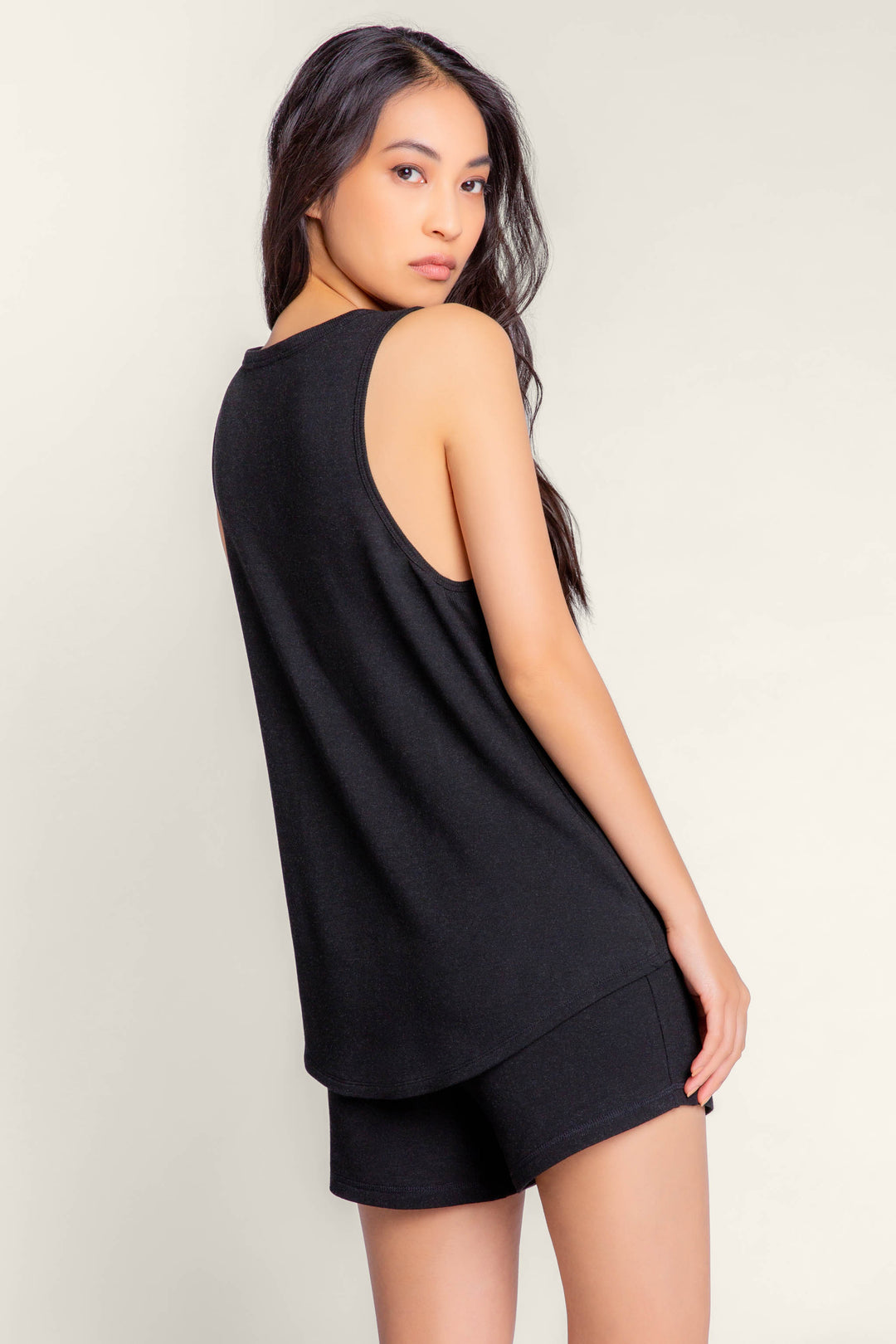 A woman with long dark hair models the P.J. Salvage Jammie Essentials Black Shorts, paired with a black sleeveless top against a light background. Shop this Final Sale style now!.