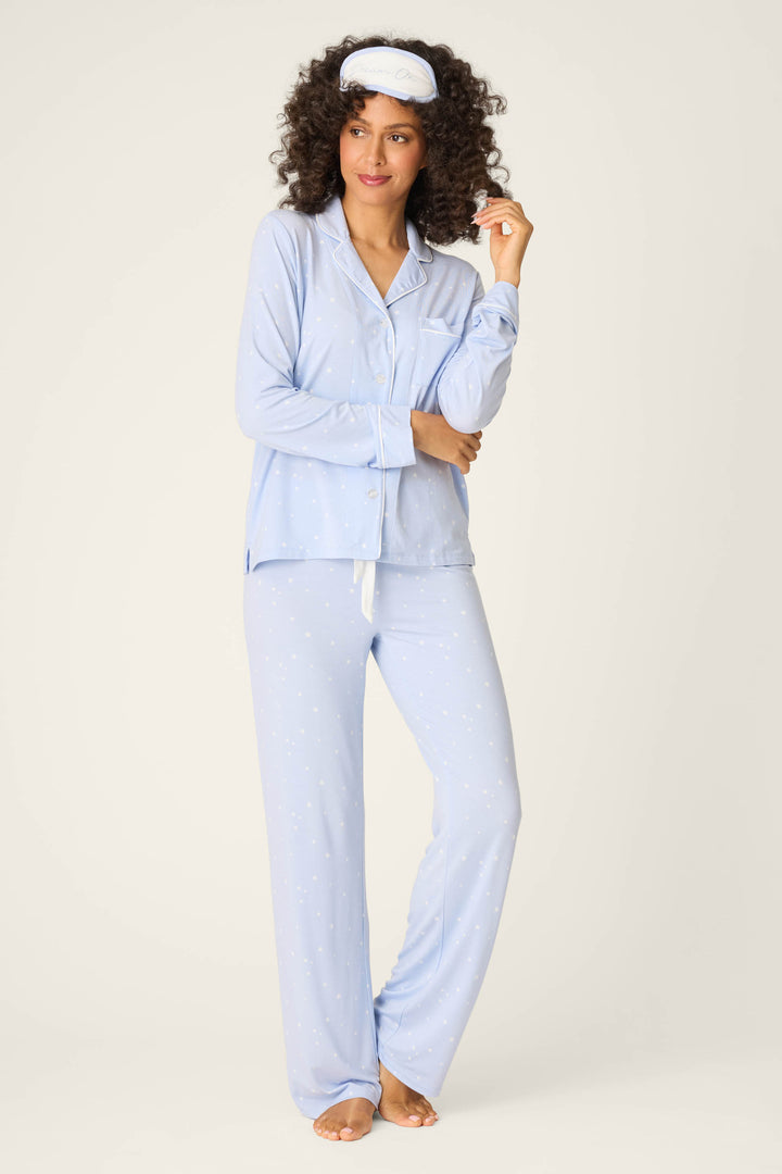 A woman wears the P.J. Salvage Modal Basics Star Print 3-Piece PJ Set—light blue, long-sleeve button-up pajamas with white star print and a matching sleep mask—standing barefoot against a plain light background.