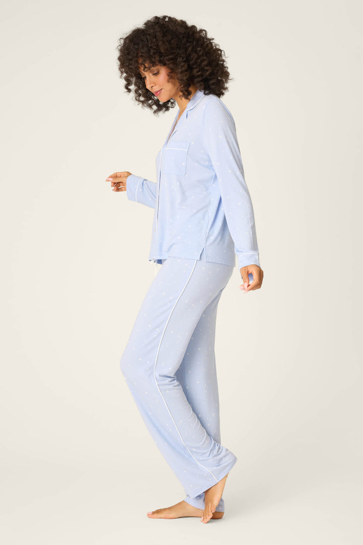 A person with curly hair stands barefoot against a plain background, facing sideways and looking down, wearing P.J. Salvage Modal Basics Star Print 3-Piece PJ Set—light blue with white dots and piping.