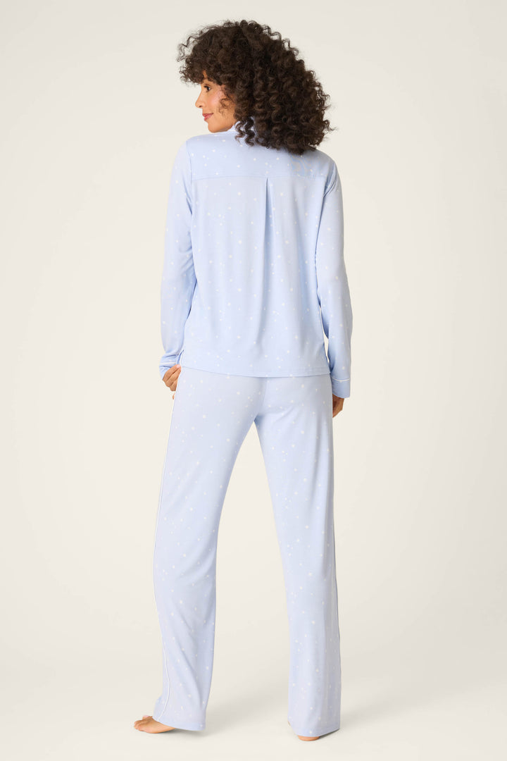 A person with curly hair stands barefoot, back to camera, wearing P.J. Salvage's Modal Basics Star Print 3-Piece PJ Set in light blue on a plain off-white background.