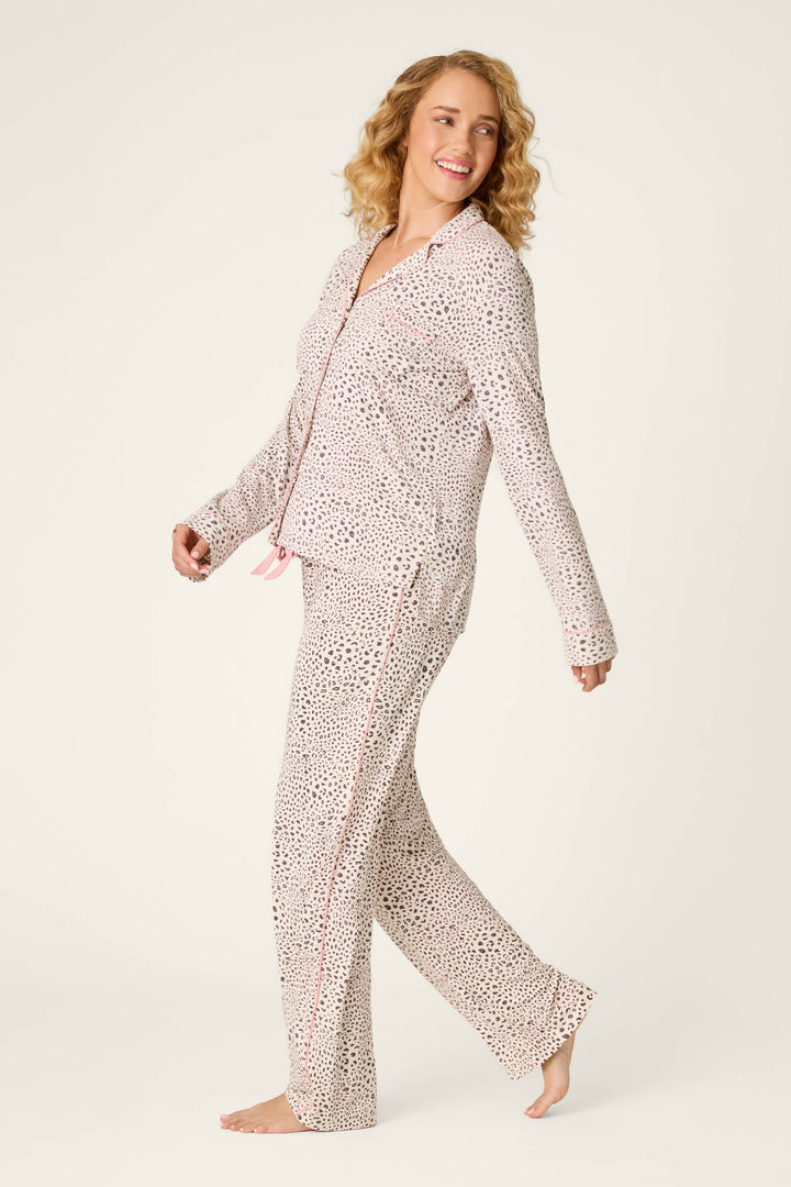 A smiling woman with curly blonde hair walks barefoot, wearing the P.J. Salvage Modal Dreams Leopard Print 3-Piece PJ Set, set against a plain off-white background.
