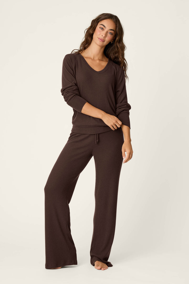 A woman with long brown hair stands barefoot, facing forward with a slight smile and arms relaxed at her sides, wearing the P.J. Salvage Textured Essentials Chocolate Brown Long Sleeve Top and matching wide-leg pants against a plain light background.