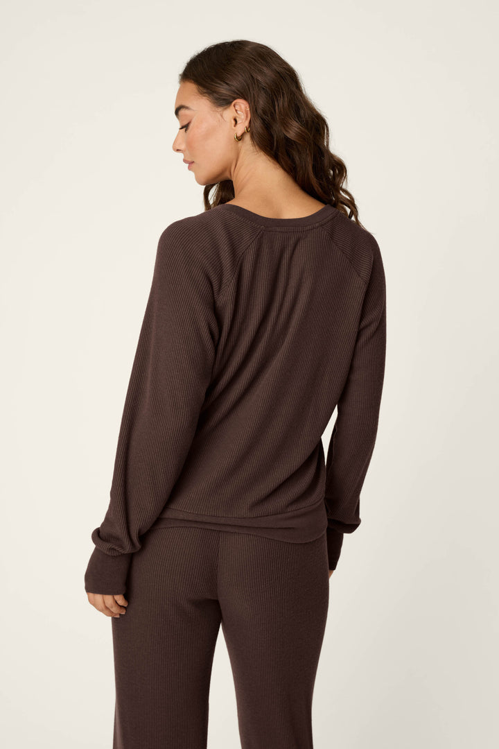A woman with long wavy hair stands against a light background, facing away from the camera, wearing the P.J. Salvage Textured Essentials Chocolate Brown Long Sleeve Top and matching pants.