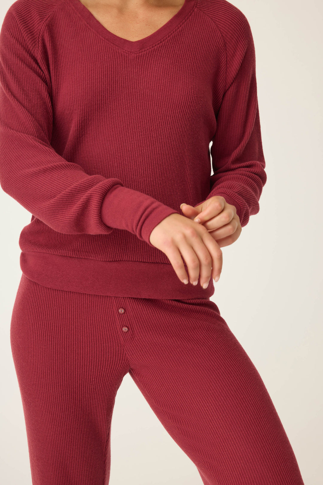 A person adjusts their sleeve while wearing the P.J. Salvage Textured Essentials Long Sleeve Top in Port, shown from shoulders to thighs against a plain background.
