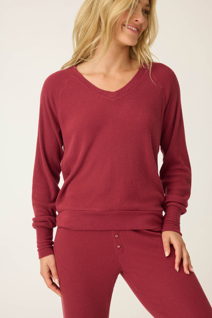 A person wears the P.J. Salvage Textured Essentials Long Sleeve Top in Port, standing against a plain light background and smiling with one hand on their hip.