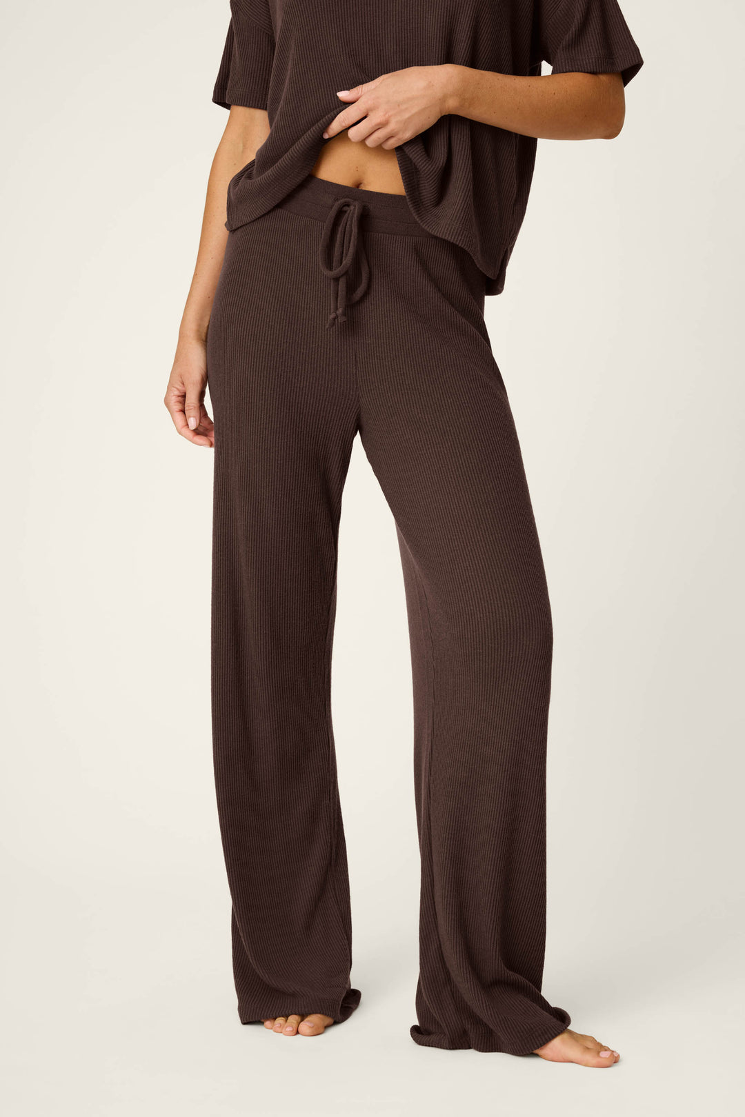 A person stands barefoot against a light background, wearing the Textured Essentials Chocolate Brown Lounge Pants by P.J. Salvage along with a matching top; their head is not visible in the image.