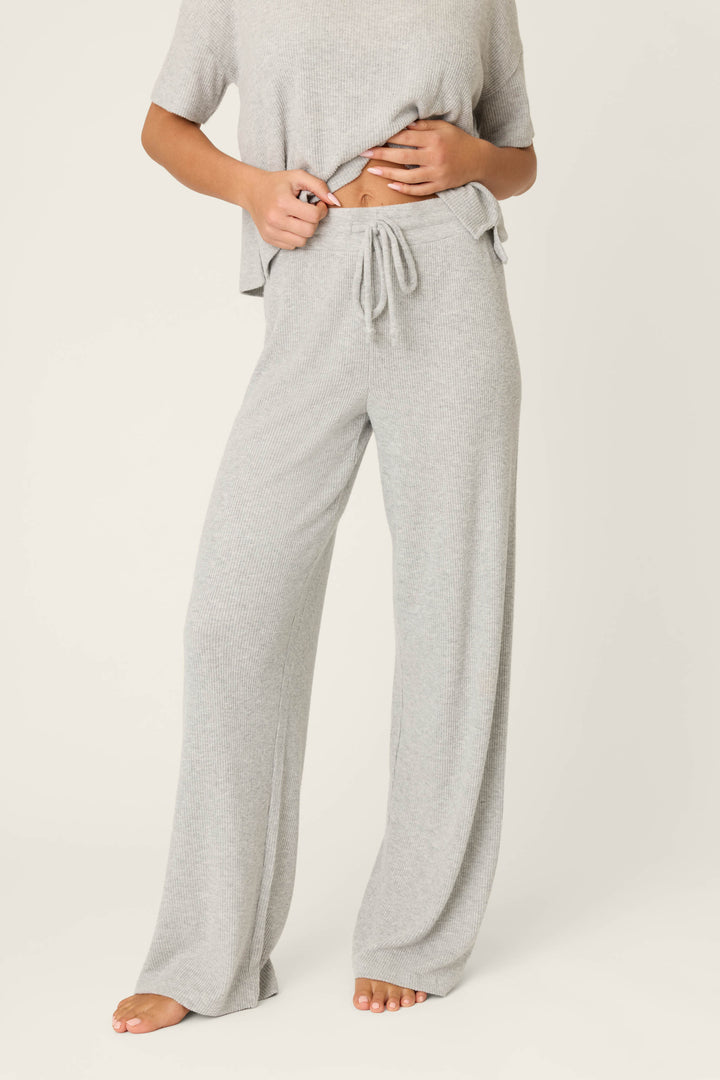 A person wearing P.J. Salvage Textured Essentials Heather Grey Open Leg Pants with a short-sleeve top. The ribbed knit loungewear set is loose-fitting; the person is barefoot and their face isn't visible.