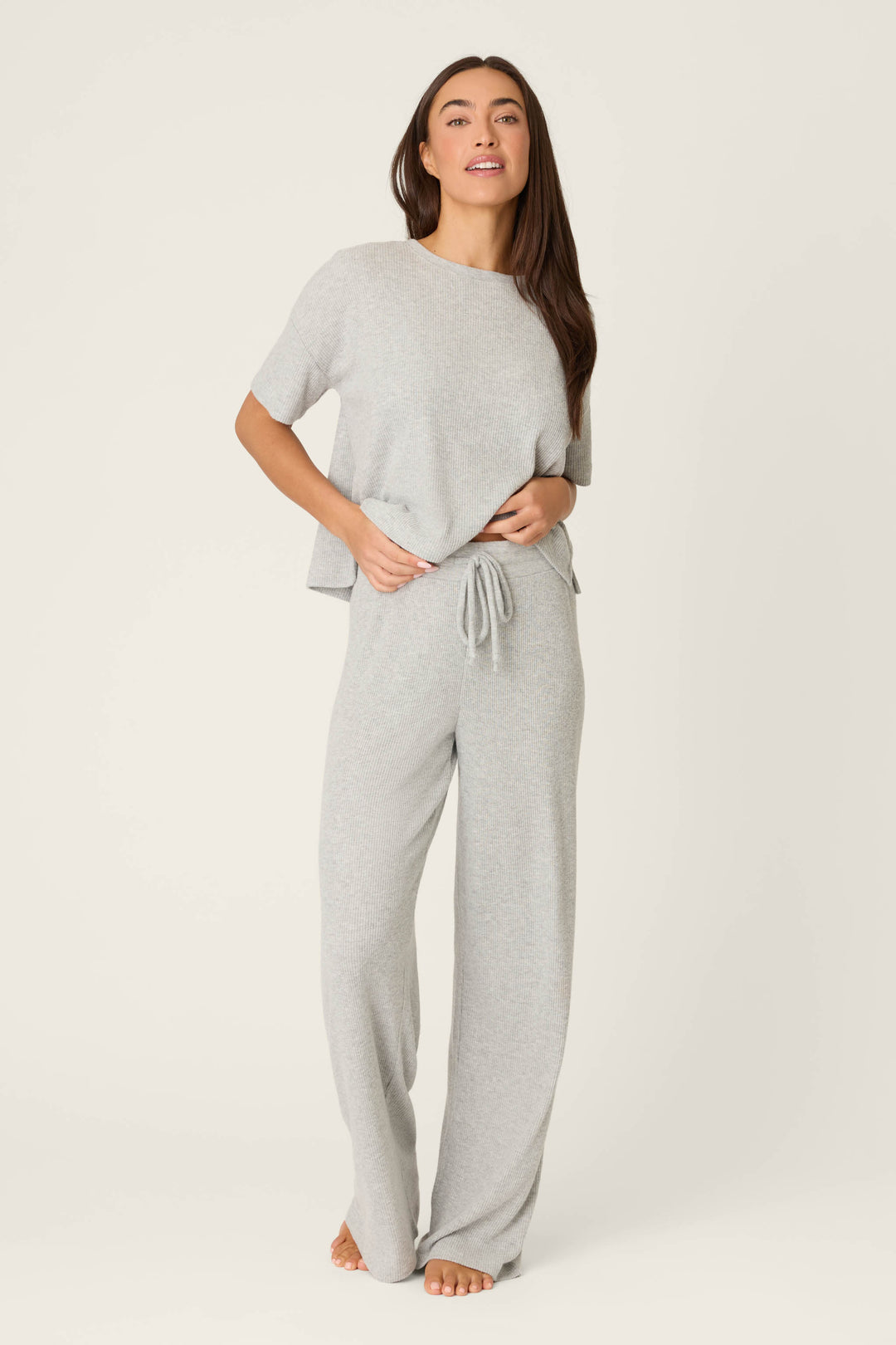 A person stands barefoot against a plain background, wearing P.J. Salvage’s Textured Essentials Heather Grey Open Leg Pants and a loose-fitting light gray short-sleeve top.