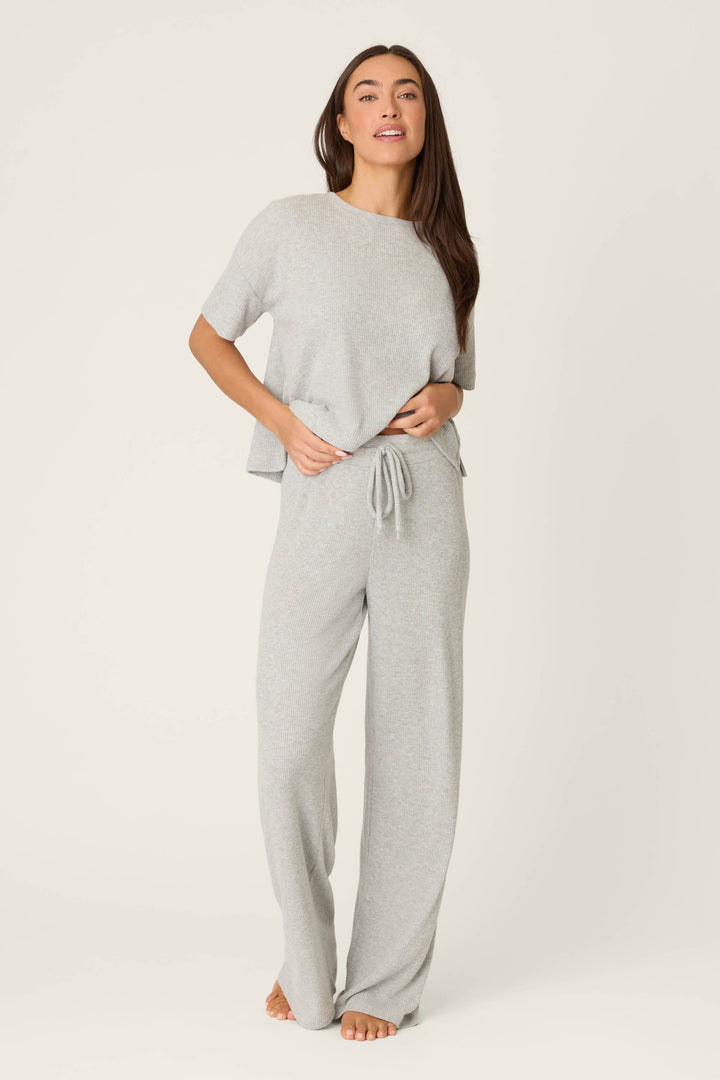 A person stands barefoot against a plain background, wearing P.J. Salvage’s Textured Essentials Heather Grey Open Leg Pants and a loose-fitting light gray short-sleeve top.