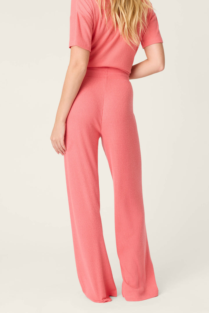 A person stands with back to camera, wearing P.J. Salvage Textured Essentials Sunset Rose Open Leg Pants and a matching pink ribbed short-sleeve top against a plain, light background.