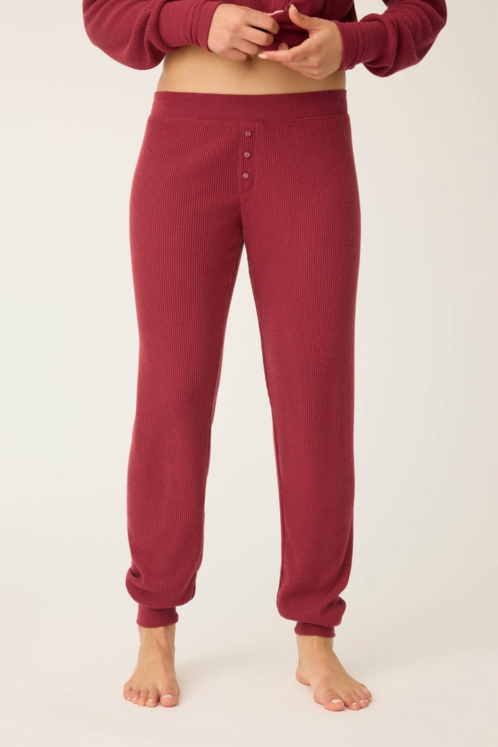 A person stands barefoot in P.J. Salvage Textured Essentials Banded Pants - Port, shown from waist to ankles against a plain background. The burgundy pants feature ribbed texture and a buttoned front.
