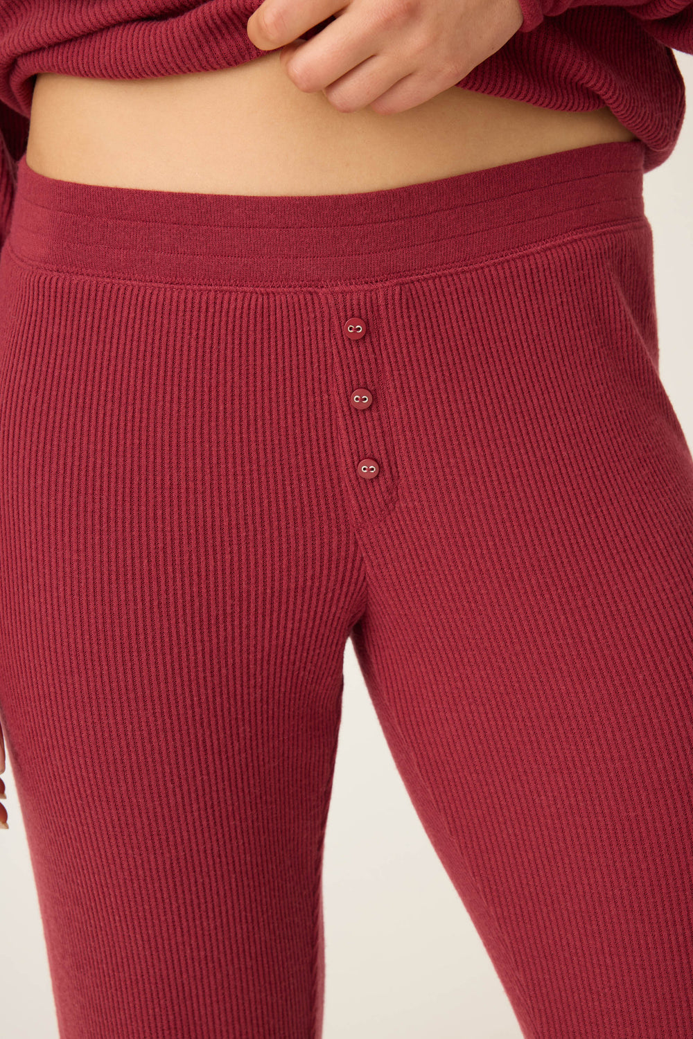Close-up of a person wearing P.J. Salvage’s Textured Essentials Banded Pants in Port, featuring ribbed, high-waisted design with a wide waistband and three front buttons. Their hand is resting near the waistband.