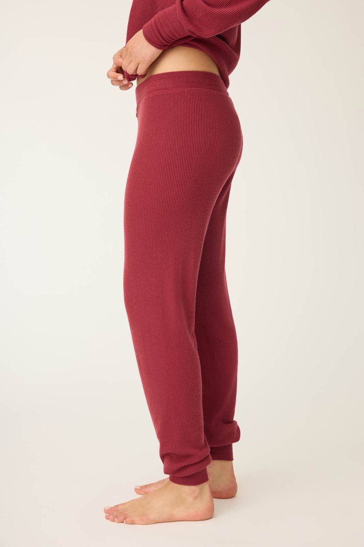 A person stands barefoot on a light surface, shown from the side, wearing P.J. Salvages Textured Essentials Banded Pants in Port with a matching long-sleeve top, adjusting the waistband.