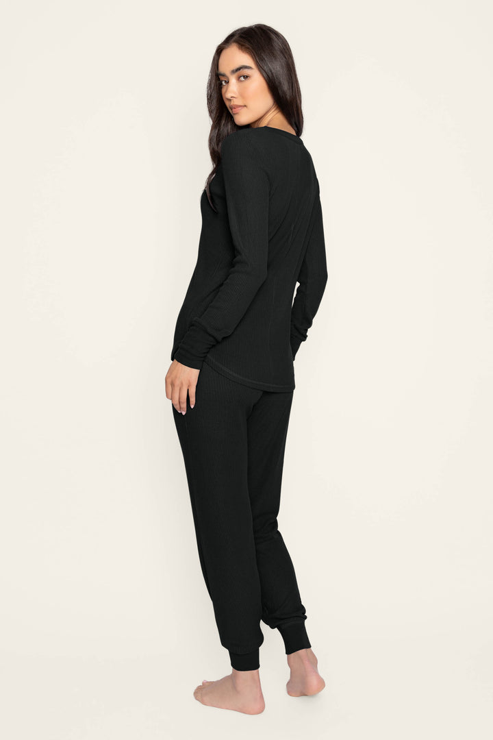 A person stands barefoot, turned sideways and glancing over their shoulder, wearing the P.J. Salvage Textured Essentials Black Lounge Set against a simple light backdrop.