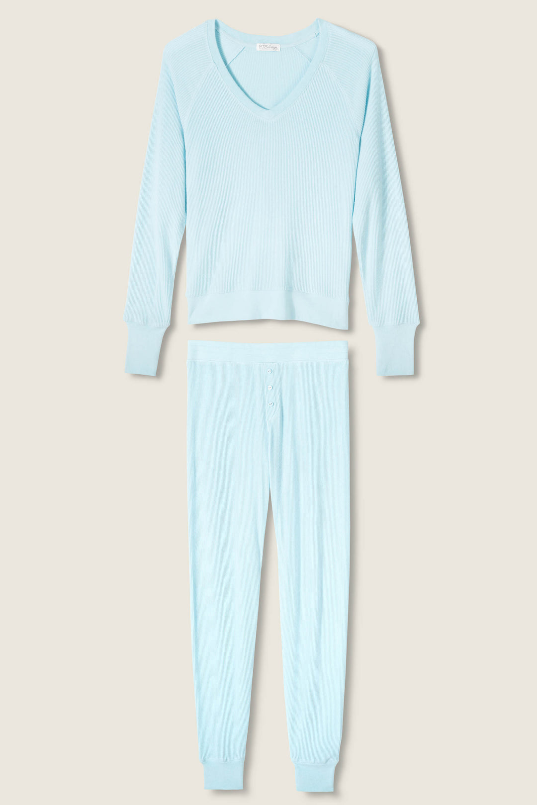 The P.J. Salvage Textured Essentials Light Sky Pants Set features a light blue ribbed V-neck long-sleeve pajama top and matching pants with button fly and cuffed ankles, shown on a neutral background.