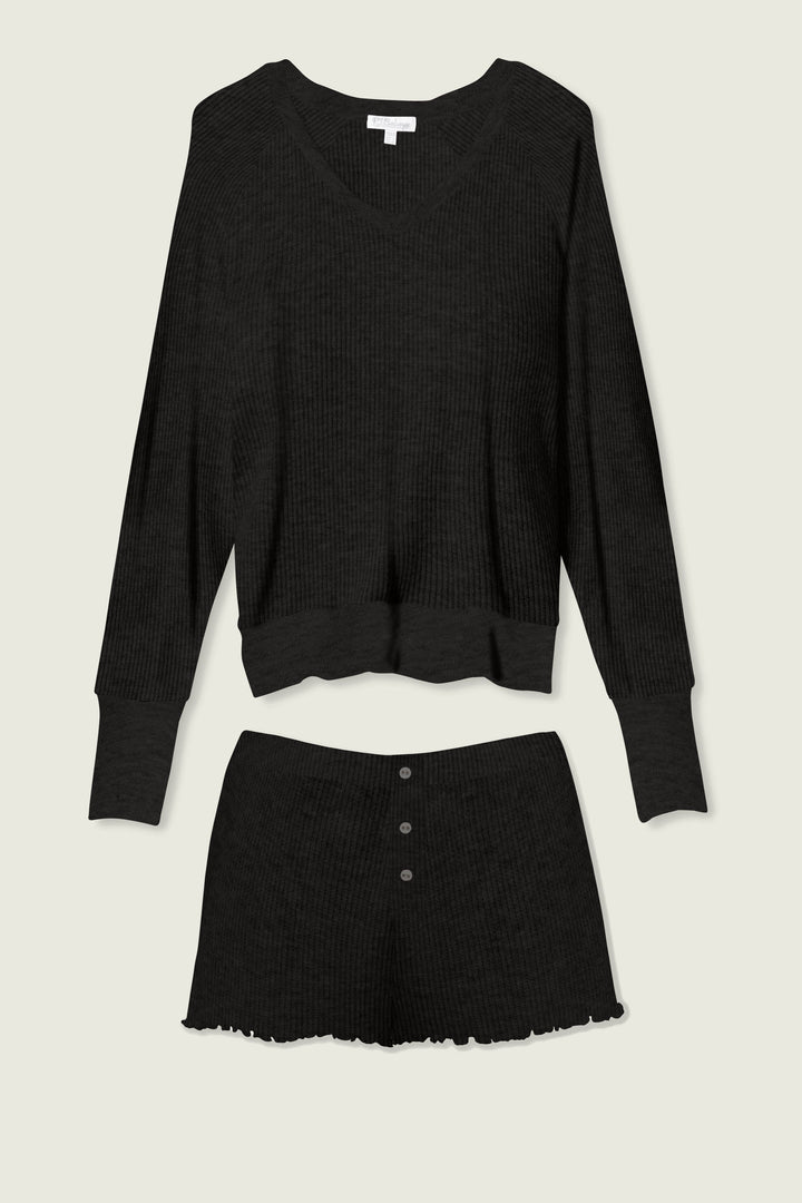The P.J. Salvage Textured Essentials Black Short Lounge Set features a ribbed knit V-neck long-sleeve top and high-waisted shorts with three buttons and a ruffled hem, shown laid flat on a light background.