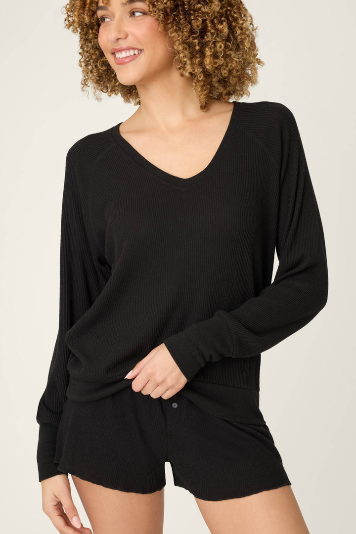 A person with curly hair smiles while wearing the P.J. Salvage Textured Essentials Black Short Lounge Set against a plain, light-colored background.