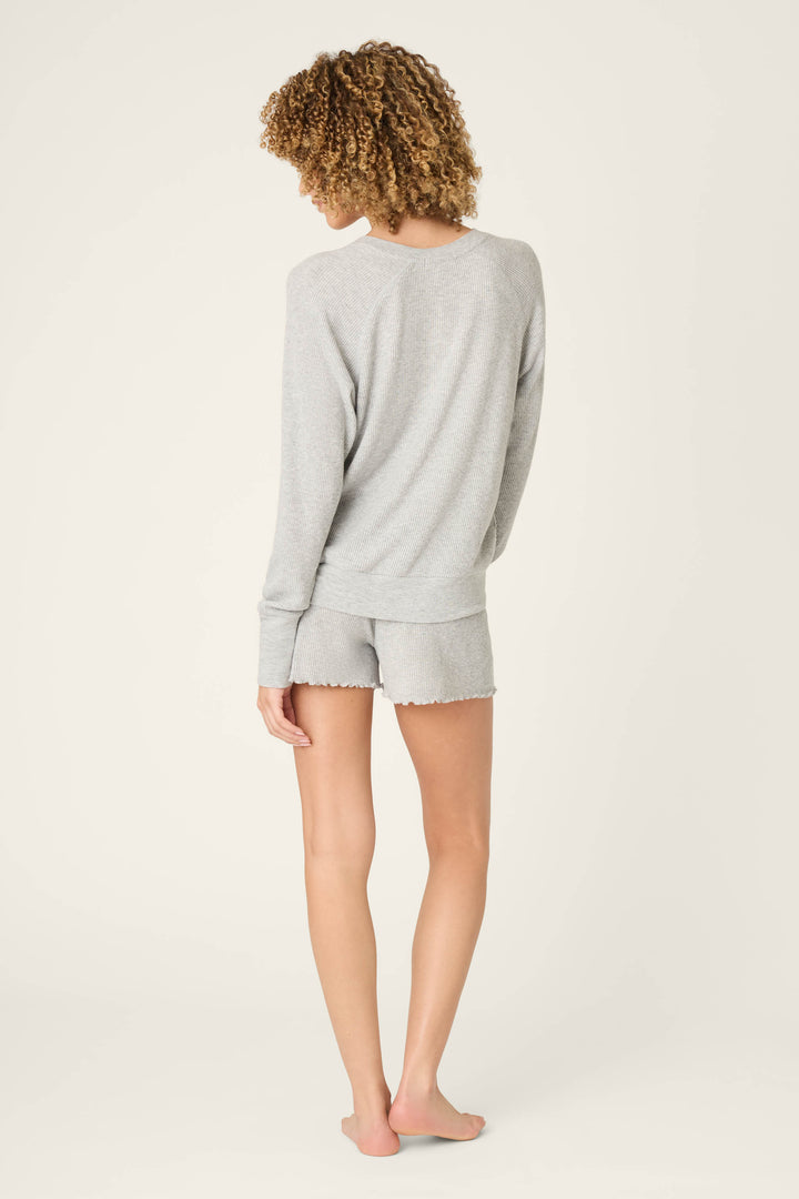 A person with curly hair stands barefoot, wearing the P.J. Salvage Textured Essentials Heather Grey Short Lounge Set against a plain off-white background.