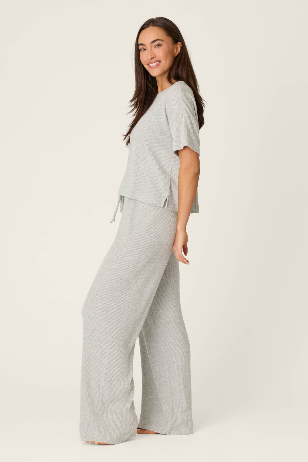 A person smiles, standing sideways, wearing the P.J. Salvage Textured Essentials Heather Grey Long PJ Set against a plain off-white background.