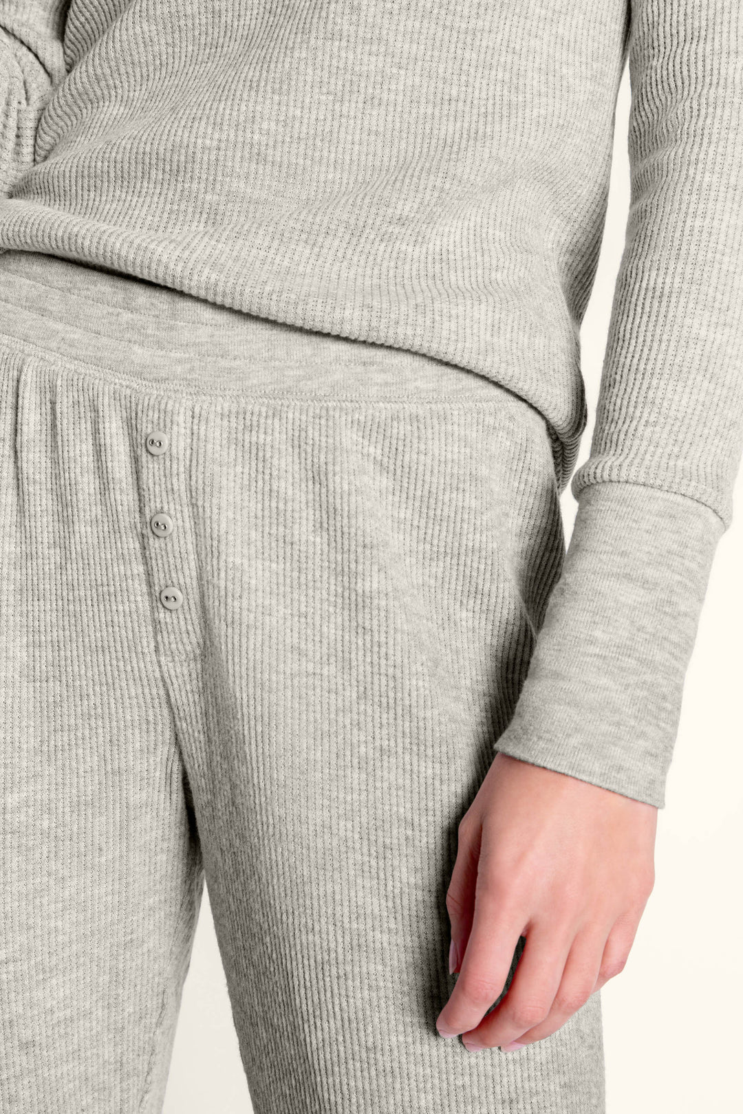 A person wears the P.J. Salvage Textured Essentials Heather Grey Long PJ Set, featuring a V-neck Henley top and loose lounge pants with button detail at the waist; only their torso and upper legs are visible.