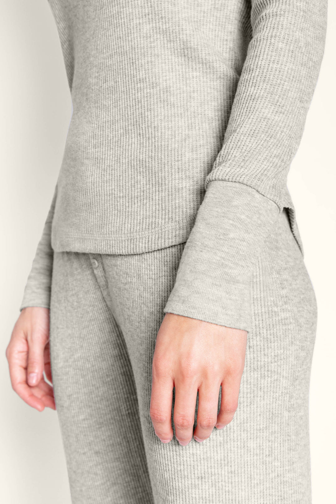 A person models the P.J. Salvage Textured Essentials Heather Grey Long PJ Set, featuring a jersey ribbed V-neck Henley top and matching lounge pants; the shot highlights their torso and upper legs with one arm relaxed at their side.