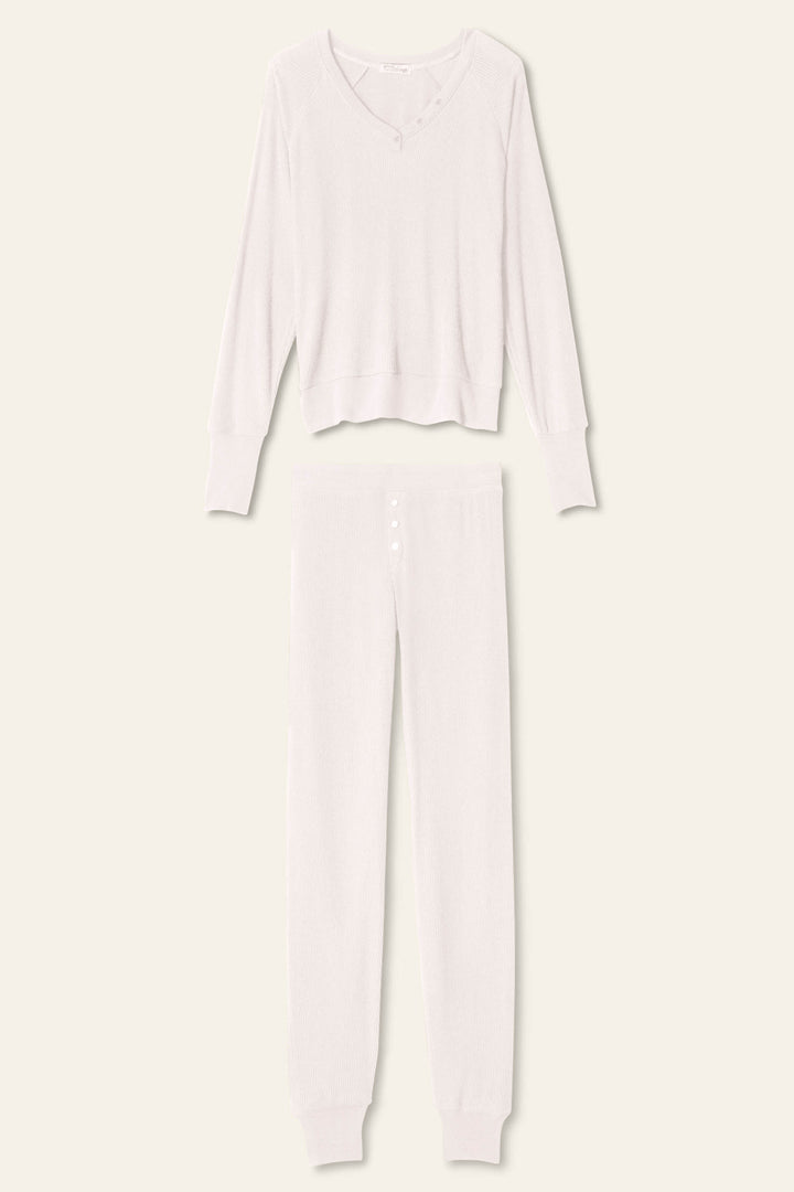 Introducing the P.J. Salvage Textured Essentials Stone Lounge Set—a coordinating light beige knit ensemble, featuring a long-sleeve Henley top with a scoop neckline and button detailing, paired with matching long pants with a buttoned front and cuffed ankles. This set is crafted from soft rib peachy jersey and beautifully displayed flat on a neutral background.