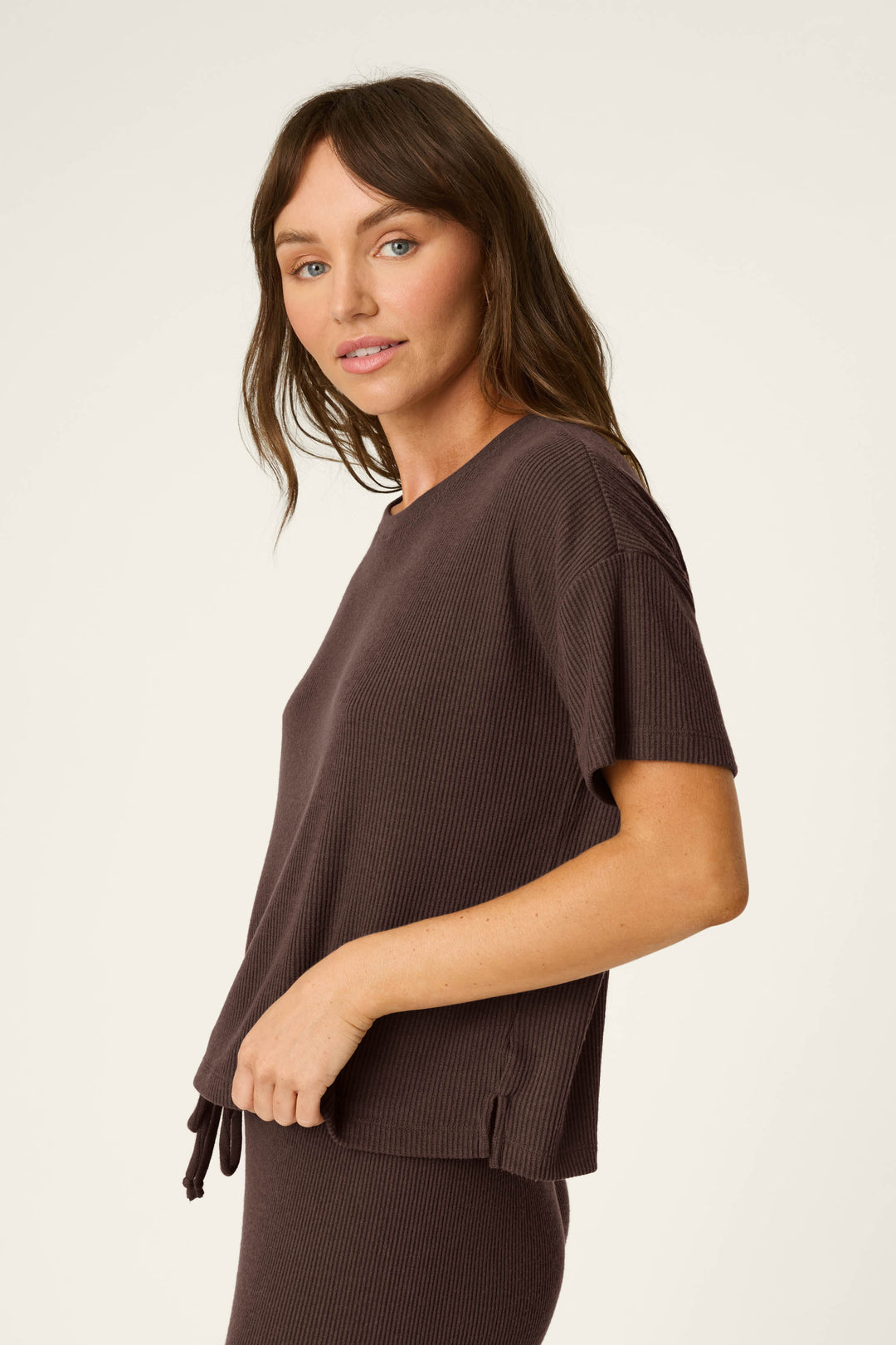 A woman with long brown hair is wearing the P.J. Salvage Textured Essentials Chocolate Brown Short Sleeve Top, paired with matching pants, standing sideways and looking at the camera against a plain light background.