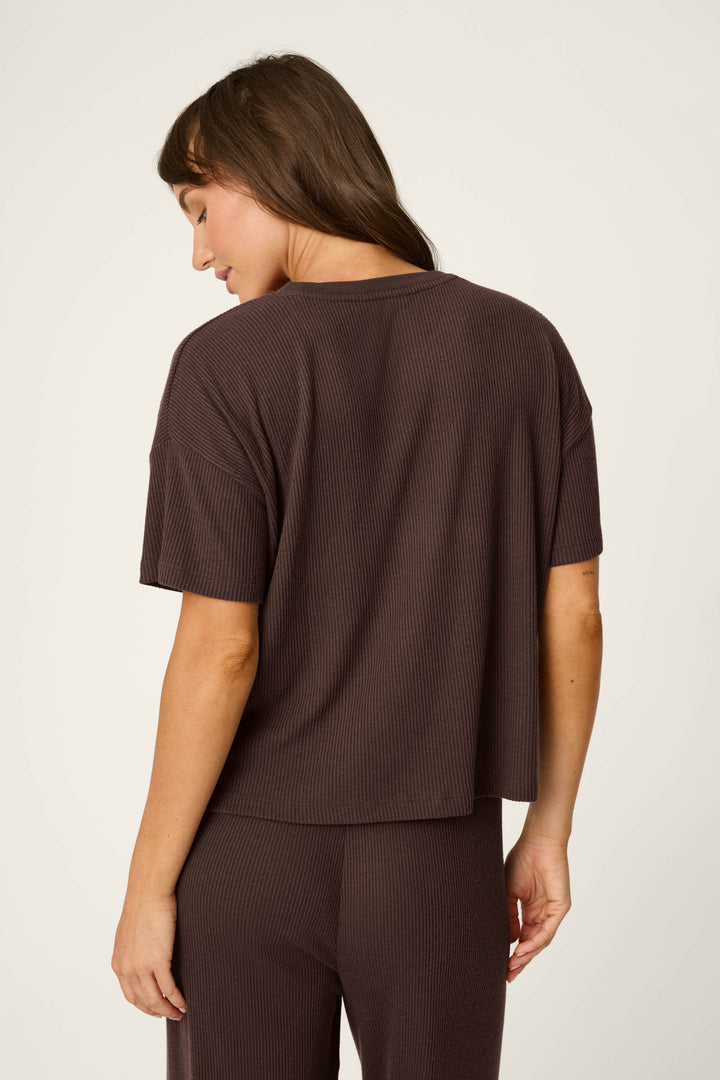 A woman stands with her back turned, wearing the P.J. Salvage Textured Essentials Chocolate Brown Short Sleeve Top and matching pants. Her head is slightly tilted down, revealing long brown hair.