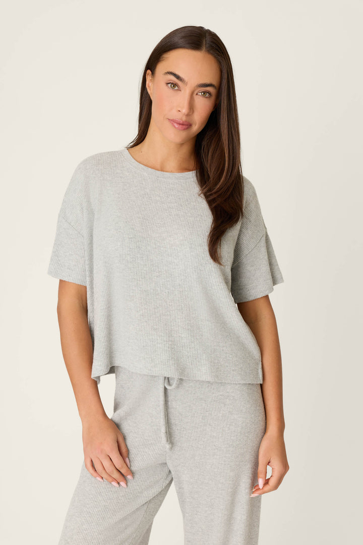 A woman with long brown hair wears the P.J. Salvage Textured Essentials Heather Grey Short Sleeve Top and matching pants, standing against an off-white background and looking at the camera with a neutral expression.