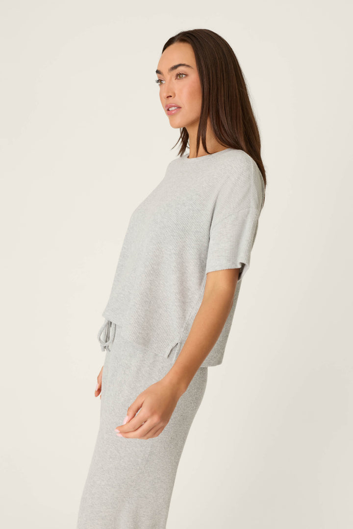 A person with long brown hair wears the P.J. Salvage Textured Essentials Heather Grey Short Sleeve Top and matching skirt, standing sideways against a plain light background, looking slightly off-camera.