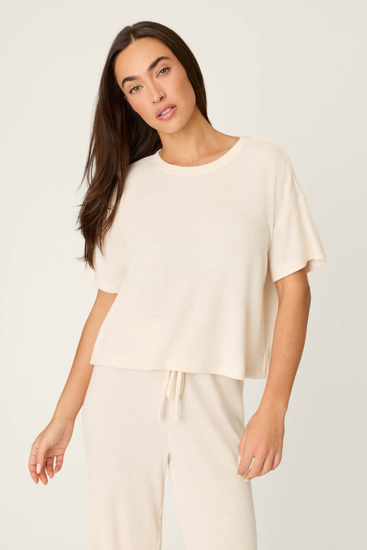 A woman with long brown hair wears the P.J. Salvage Textured Essentials Stone Short Sleeve Top, standing against a plain light background and gazing at the camera with a neutral expression.