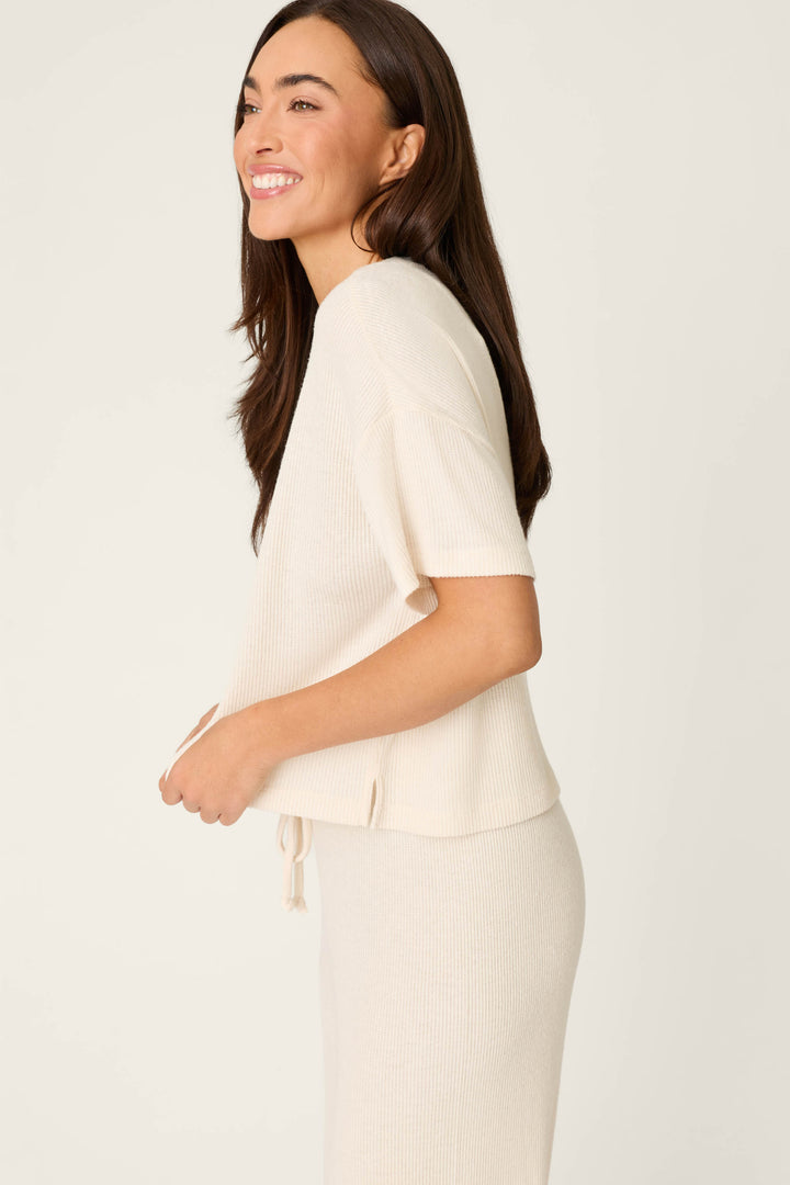 A woman with long brown hair stands sideways, smiling. She wears the P.J. Salvage Textured Essentials Stone Short Sleeve Top, paired with a matching skirt against a plain off-white background.