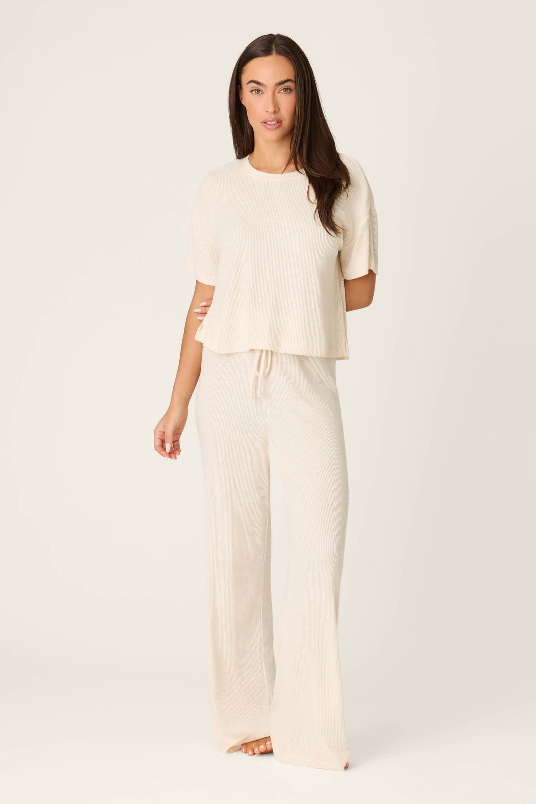 A woman stands facing forward wearing the P.J. Salvage Textured Essentials Stone Short Sleeve Top with matching wide-leg pants featuring a drawstring waist, set against a plain light background.