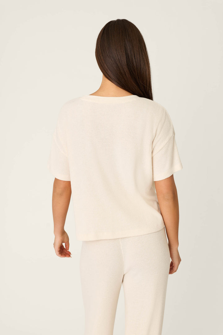 A woman with long brown hair, seen from behind, wears the P.J. Salvage Textured Essentials Stone Short Sleeve Top and matching pants against a plain off-white background.