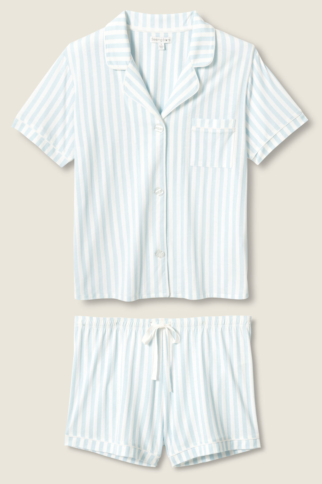 The Blue Stripe PJ Set by P.J. Salvage features a short-sleeve, button-up top with a chest pocket and matching drawstring shorts, both in light blue and white vertical stripes, displayed flat on a beige background.