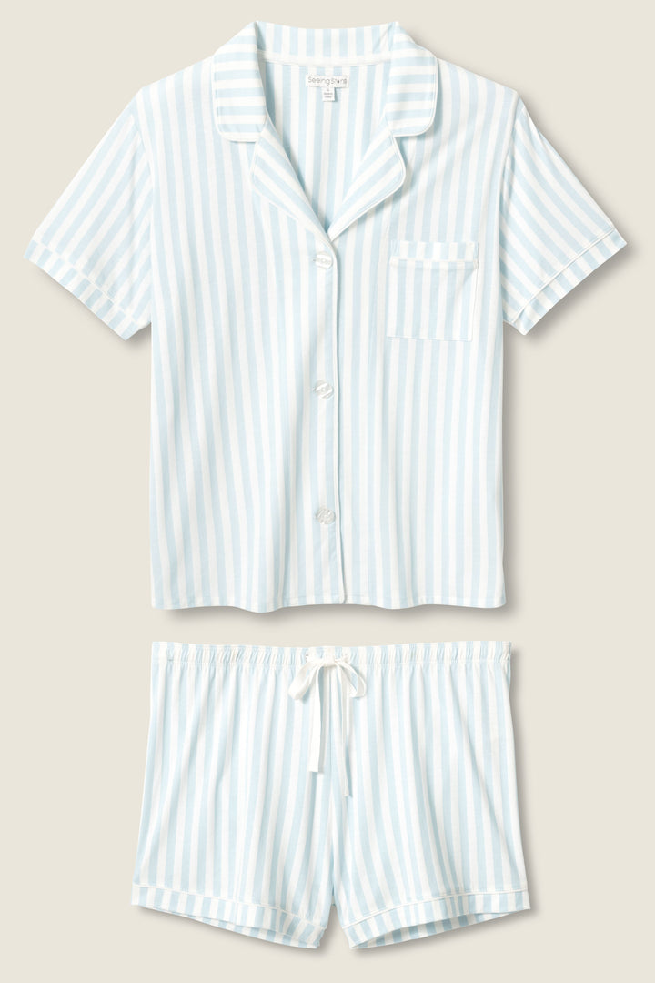 The Blue Stripe PJ Set by P.J. Salvage features a short-sleeve, button-up top with a chest pocket and matching drawstring shorts, both in light blue and white vertical stripes, displayed flat on a beige background.
