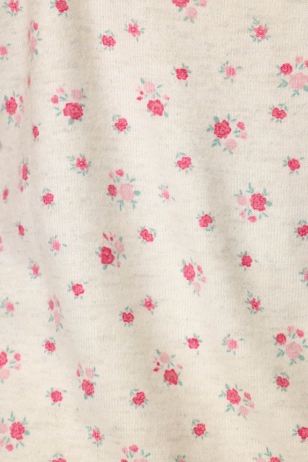 A close-up of a cream-colored fabric with a delicate, small-scale pink and red floral print.