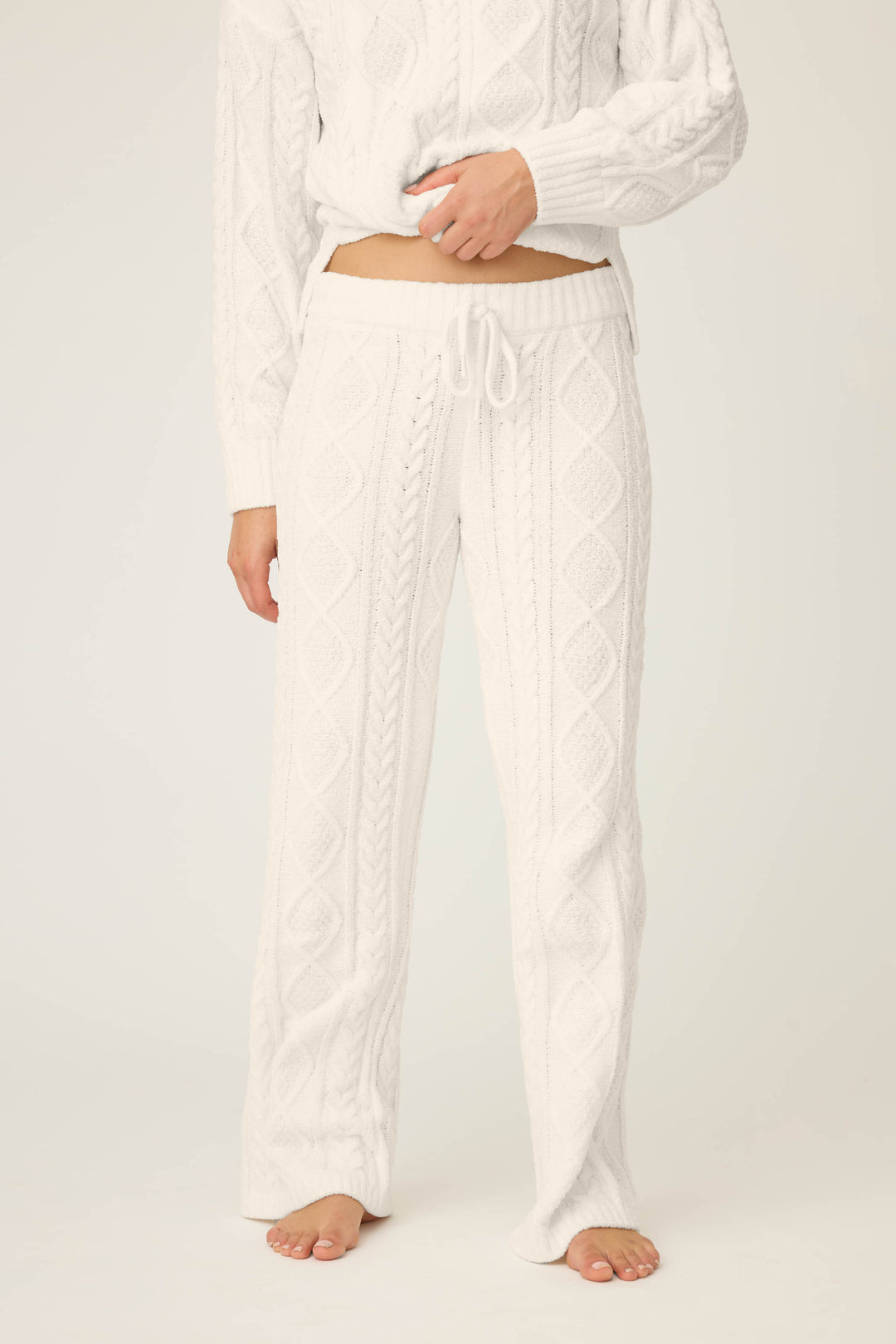 A person models the P.J. Salvage PJ SET CABLE CREW LOUNGE—matching white cable knit sweater and drawstring pants—standing barefoot against a plain light background, with only the lower face and body visible.