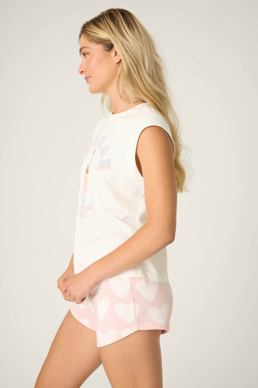 Side profile of model wearing ‘Sundae Best’ ivory muscle tee and pink shorts with bold white heart print.