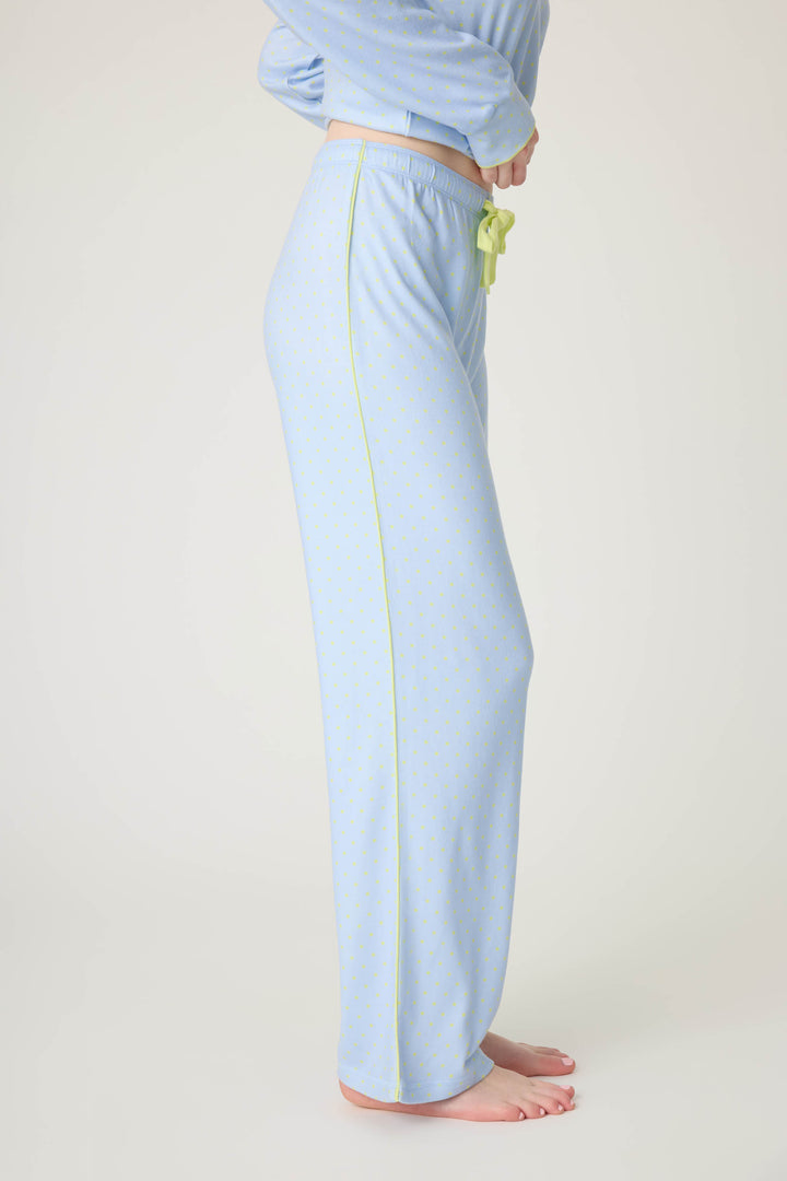A person stands barefoot in profile, wearing P.J. Salvage’s Beautiful Life Polka Dot Open Leg Pant in light blue with a subtle dotted pattern, yellow piping along the seam, and a green drawstring; the matching top is partially visible.