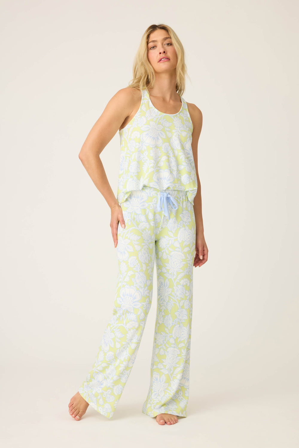 A woman stands barefoot against a plain background, wearing the P.J. Salvage Beautiful Life Floral Print PJ Set—a sleeveless, loose-fit pajama set with wide-leg pants and matching tank top. She looks relaxed with her hair down.