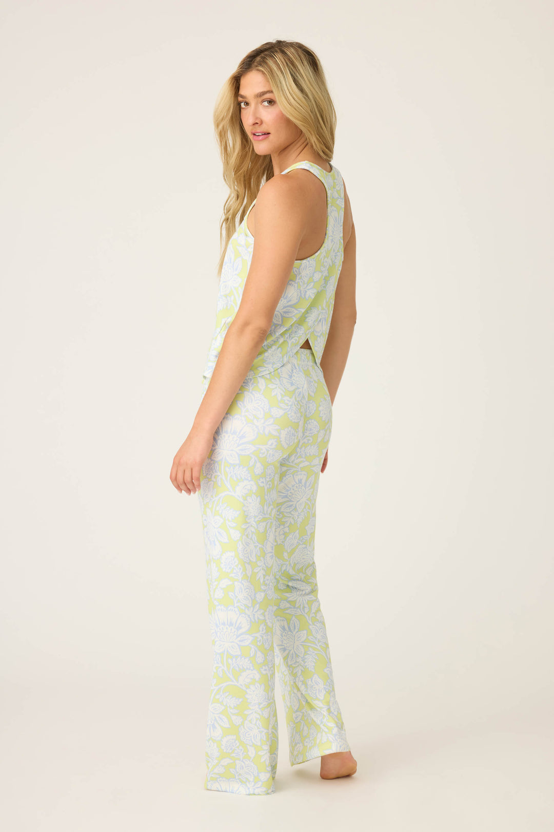 A woman with long blonde hair models the P.J. Salvage Beautiful Life Floral Print PJ Set, standing barefoot on a plain light background and looking over her left shoulder at the camera.